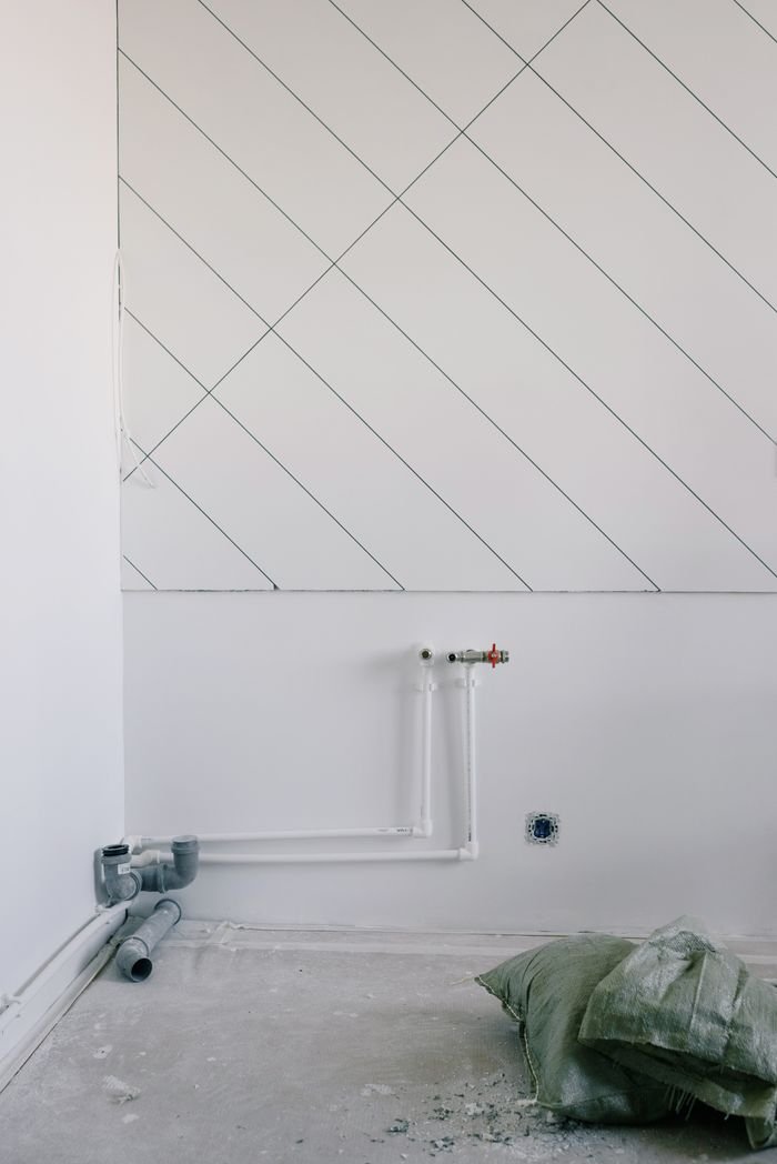 services-01 Long thin black slanted lines on white wall over pipes of radiator and litter and pillows on dirty floor in empty room